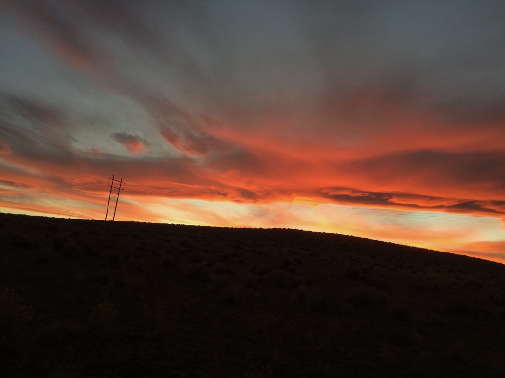 A gorgeous orange-and-red sunset glows in the Nevada desert above a small hill draped in shadows.